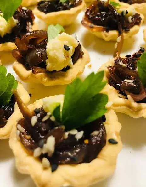 Tartaletas de cebolla caramelizada con sésamo y perejil, servidas en bandeja