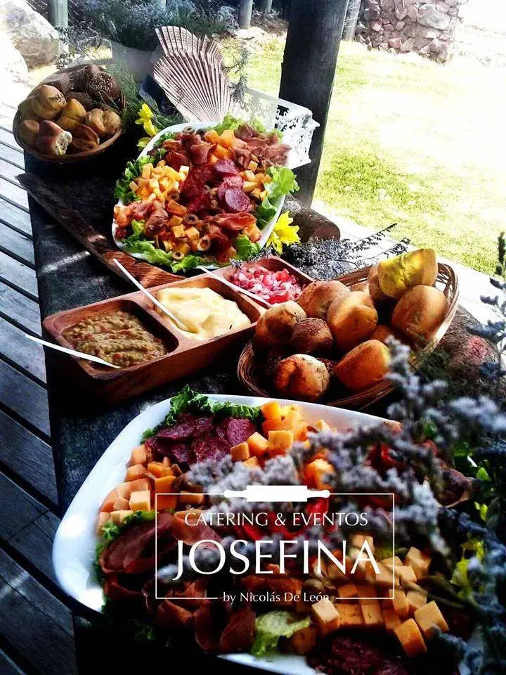 Mesa de bocaditos al aire libre con fuentes de fiambres y quesos, panes artesanales y salsas