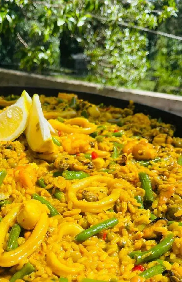 Paellera grande al aire libre con aros de calamar, chauchas y limón