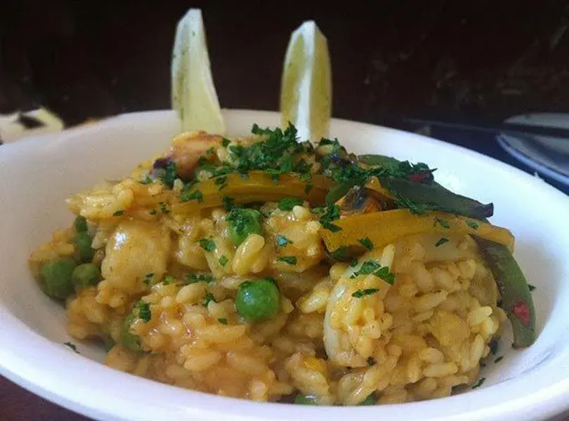 Plato de paella servido con arvejas, morrones y gajos de limón